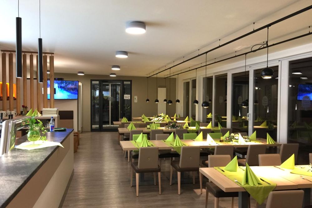 Bild des Gastraums mit Tischen entlang der Fensterfront im Restaurant in Baden-Württemberg, gestaltet von Bäuerlein Objektdesign.